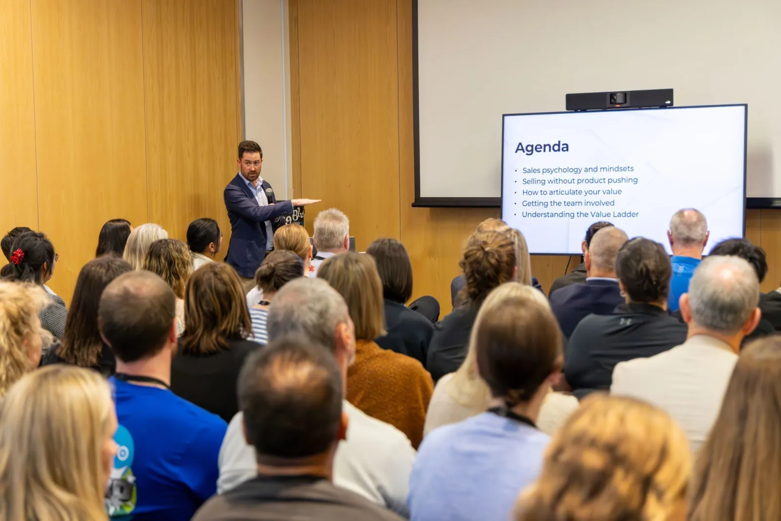 Brad Turville presenting to a full room of accountants. The slide on screen reads: Agenda. Sales psychology and mindsets. Selling without product pushing. How to articulate your value. Getting the team involved. Understanding the Value Ladder.